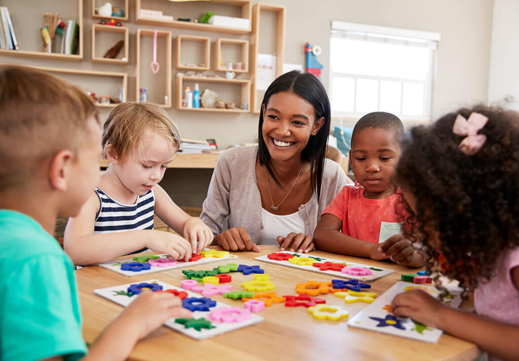A preschool teacher interacting with children playing with shapes in a table.