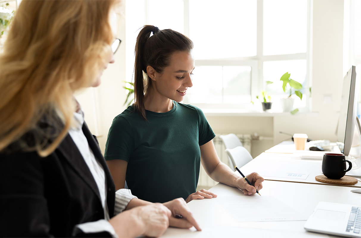 A Female mentor training a young female intern at office workplace