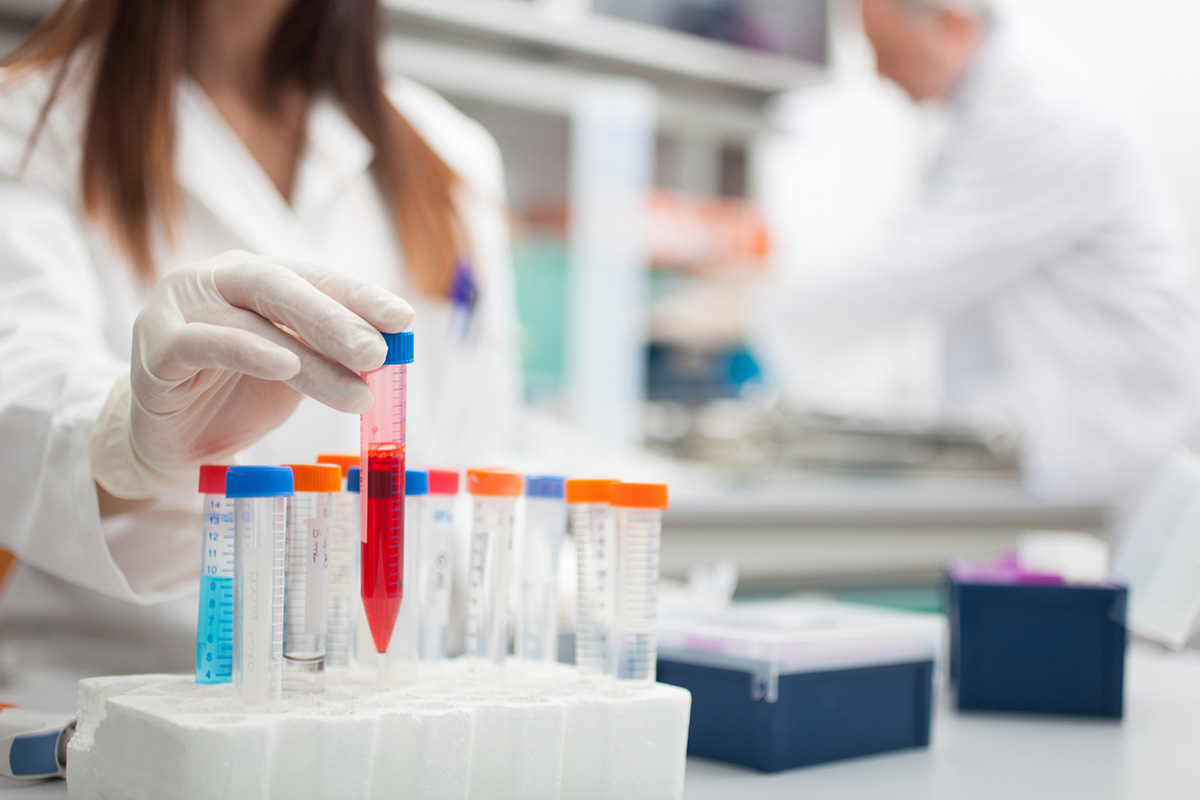 Scientist in a lab working with test tubes. A tube with red liquid is being lifted out of the test tube holder.